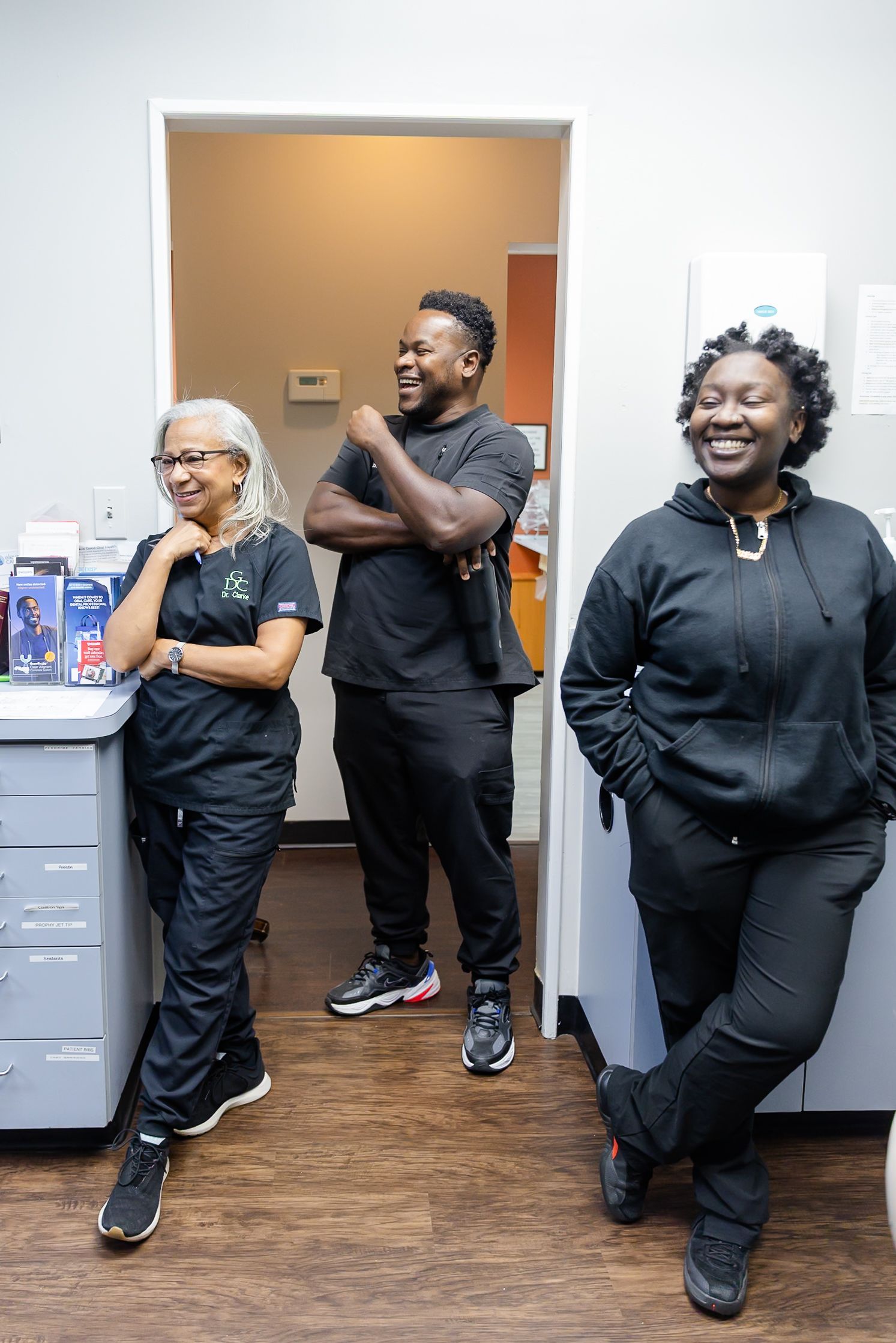 Three people in black scrubs laugh in a brightly lit office.