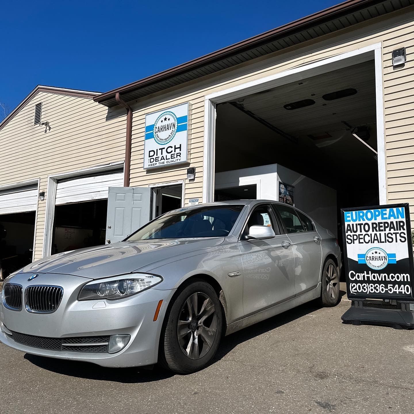 A silver car is parked in front of a car repair shop