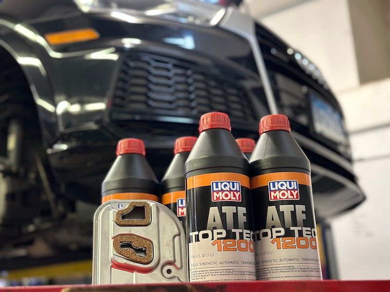 Bottles of liqui moly ate are sitting on a shelf in front of a car.