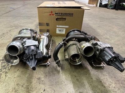 Two turbochargers are sitting next to each other in front of a box.