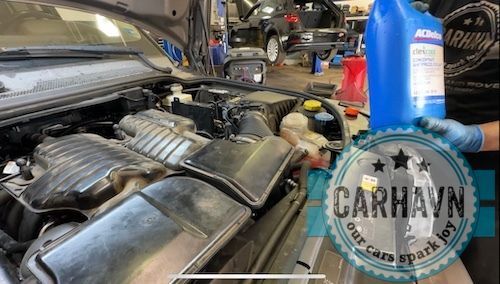 A person is holding a bottle of oil next to a car engine.