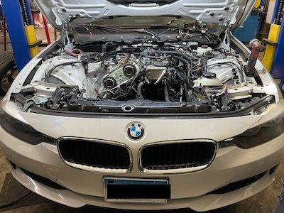 A white bmw with the hood open is sitting on a lift in a garage.