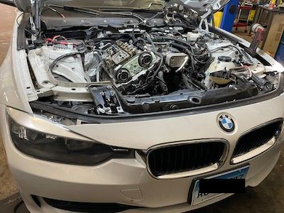 A white bmw with its hood open in a garage.