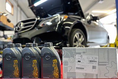 A mercedes benz is sitting on a lift in a garage next to bottles of oil.