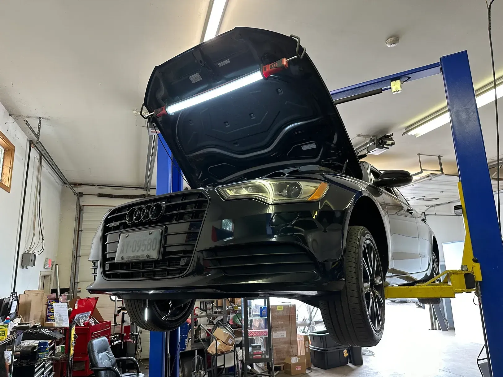 A car is on a lift in a garage with the hood open.
