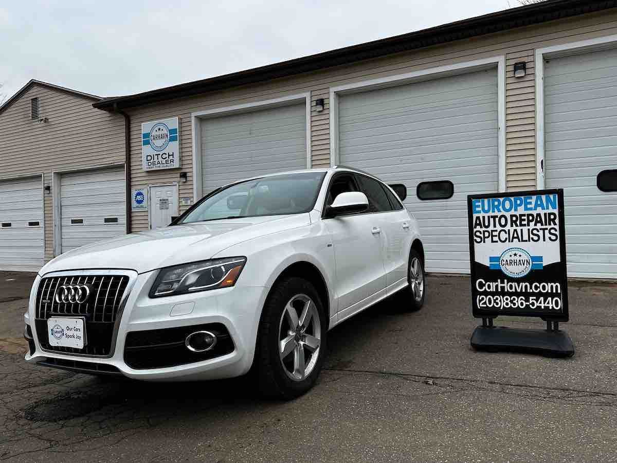 A white car is parked in front of a building next to a sign that says european auto repair specialists.