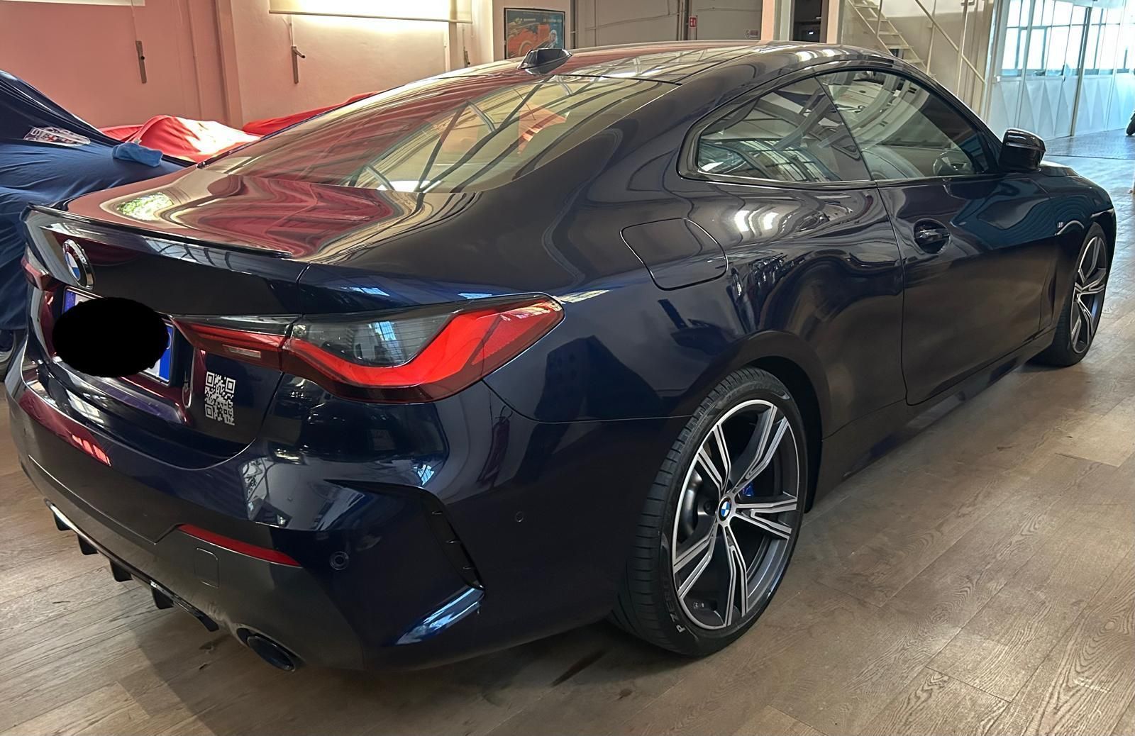 Vista posteriore, di tre quarti, di una BMW Serie 4 coupé blu scuro parcheggiata all'interno di un garage ben illuminato.