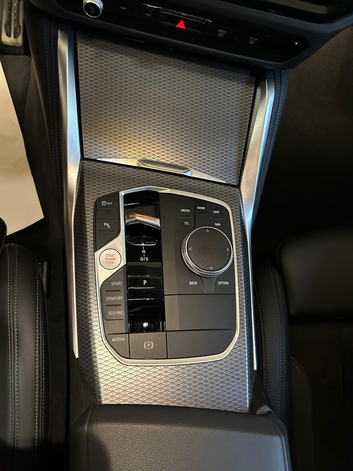 Console centrale di un veicolo moderno con leva del cambio, pulsante di avviamento del motore e manopola di controllo del sistema di infotainment.