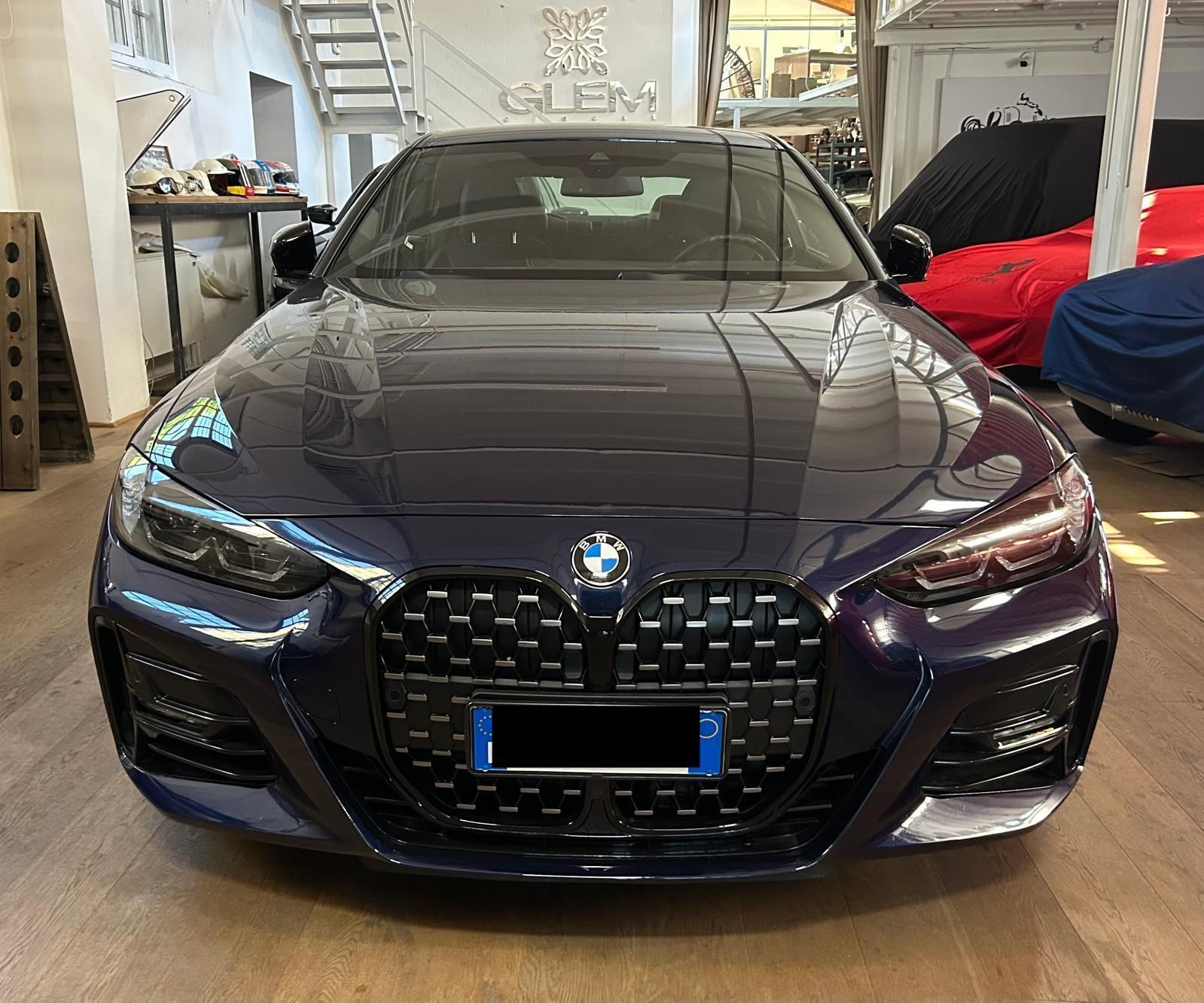 Una BMW Serie 4 coupé blu scuro parcheggiata all'interno di un'officina, con una grande griglia anteriore verticale.