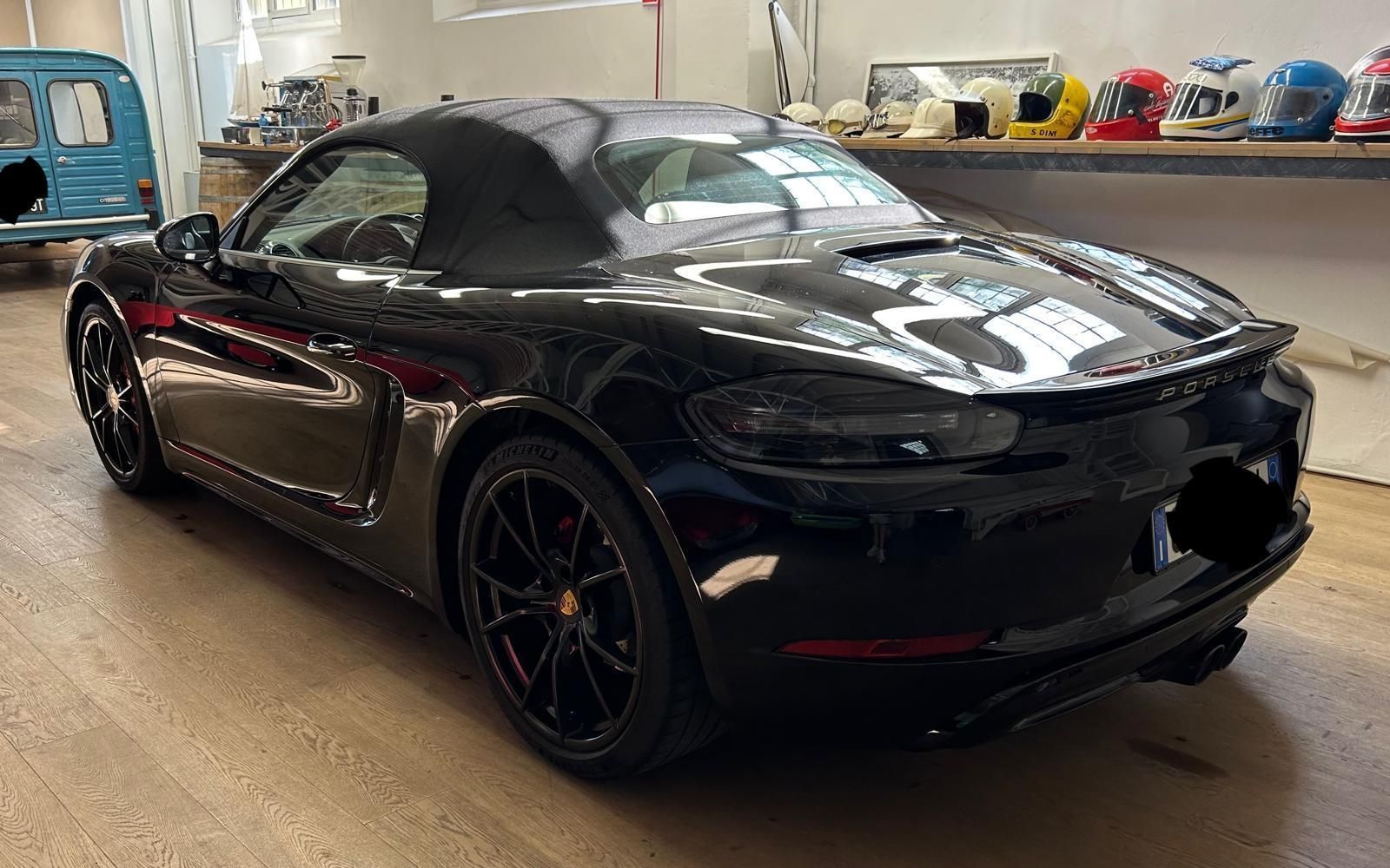 Una Porsche decappottabile nera parcheggiata all'interno di uno showroom, con una fila di caschi da corsa su uno scaffale sullo sfondo.