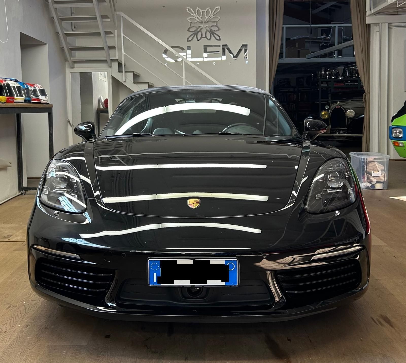 Una Porsche nera parcheggiata all'interno di uno showroom con una scala bianca sullo sfondo.