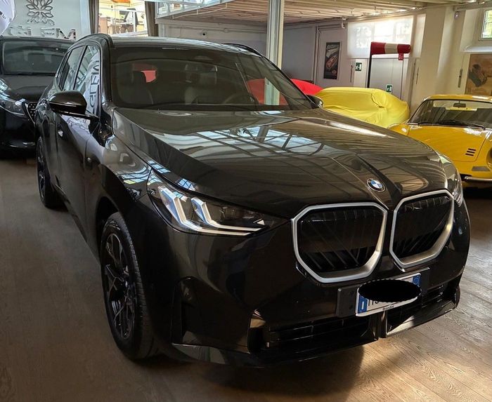 Una BMW i3 elettrica bicolore bianca e nera parcheggiata all'interno di uno showroom, con un'auto rossa e un'auto nera sullo sfondo.