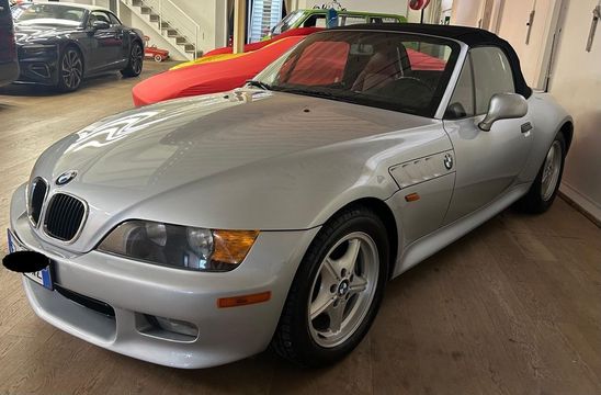 Una BMW Z3 cabriolet color argento parcheggiata all'interno di un garage accanto a un veicolo coperto di rosso.
