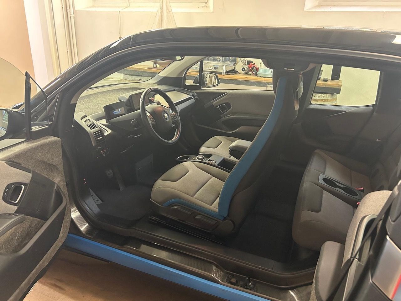 Interno di un'auto con sedili rivestiti in tessuto grigio, finiture blu, volante e cruscotto digitale.