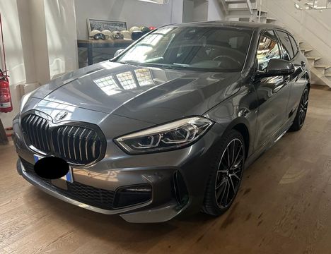 Una BMW Serie 1 hatchback grigia parcheggiata all'interno su un pavimento di legno chiaro.