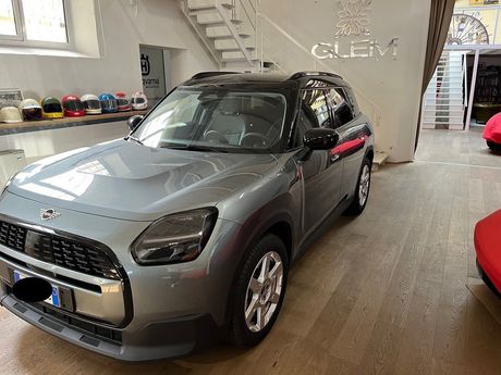 Un SUV Range Rover color argento parcheggiato all'interno di uno showroom, con sullo sfondo auto coperte da teli rossi.