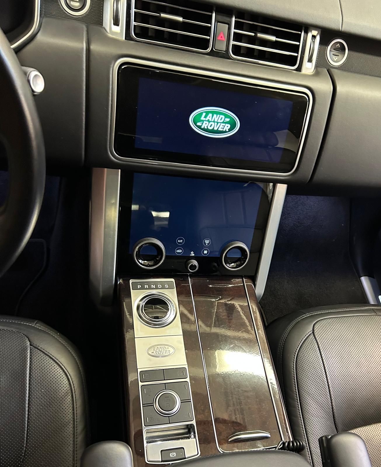 Vista interna del cruscotto di una Land Rover che mostra due touchscreen, una manopola per la selezione delle marce e una console centrale con finitura effetto legno.