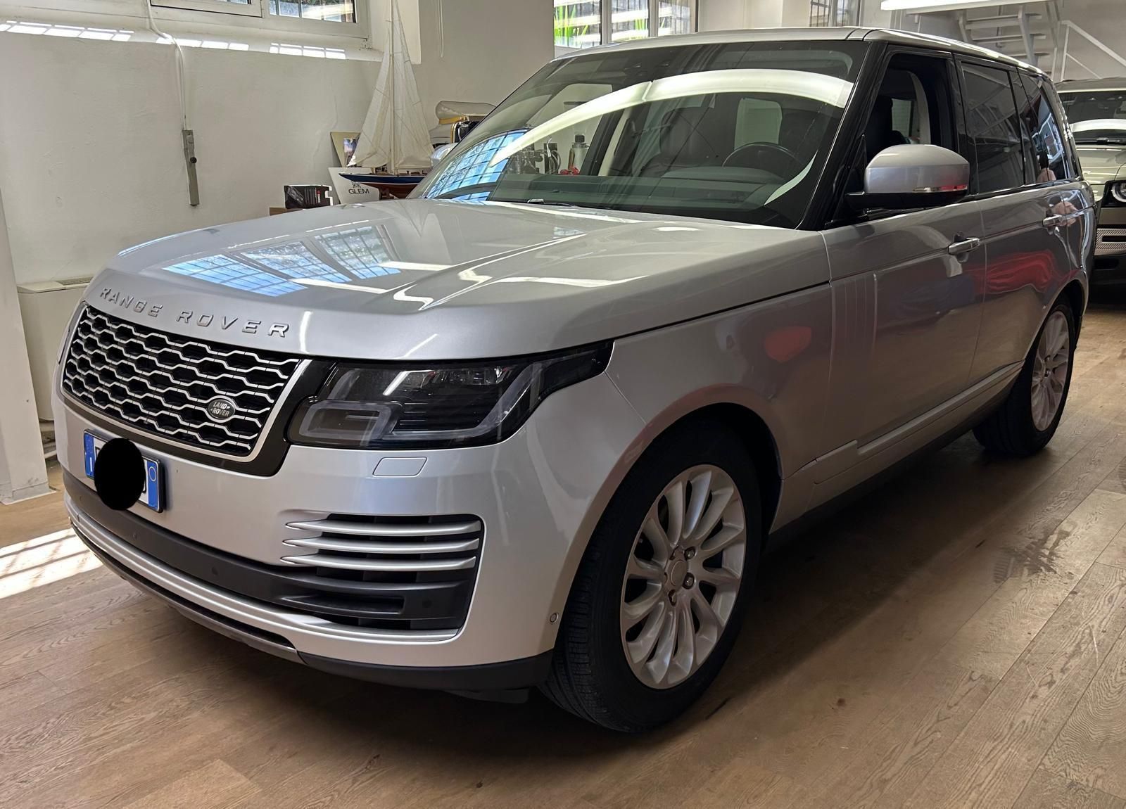 Un SUV Range Rover color argento parcheggiato all'interno di un edificio, su un pavimento effetto legno, visto dal lato del passeggero anteriore.