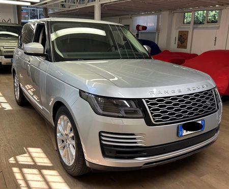 Un SUV Range Rover color argento parcheggiato all'interno di uno showroom, con sullo sfondo auto coperte da teli rossi.
