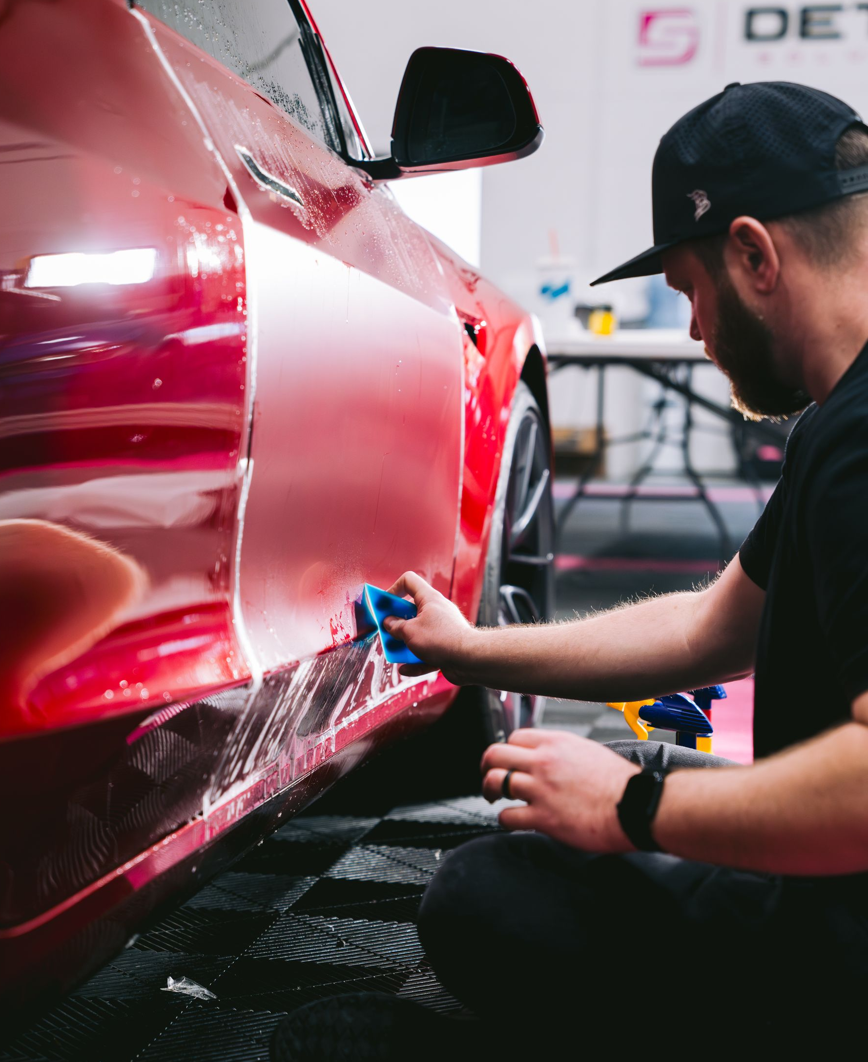 A person wearing black gloves is polishing the hood of a red car.