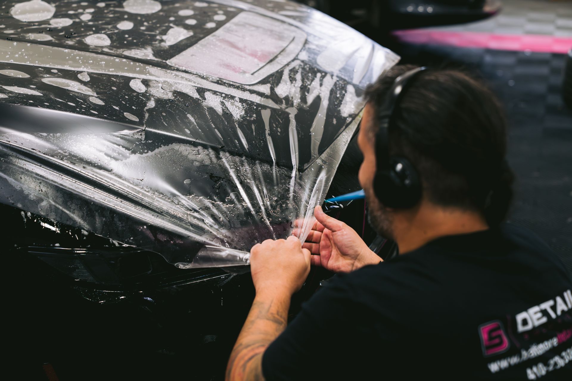 A man is wrapping a red car in plastic
