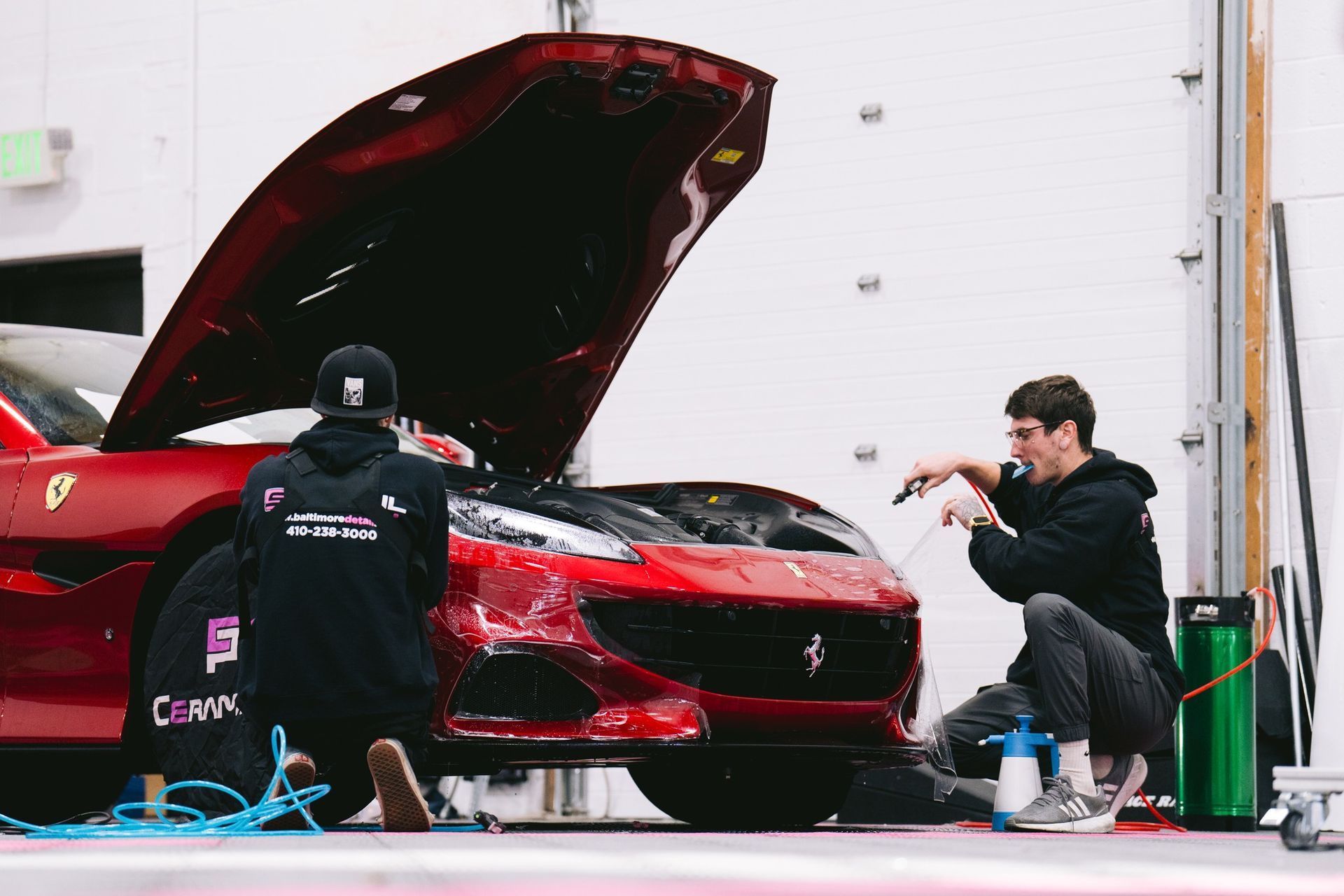 Two men are working on a red sports car in a garage.