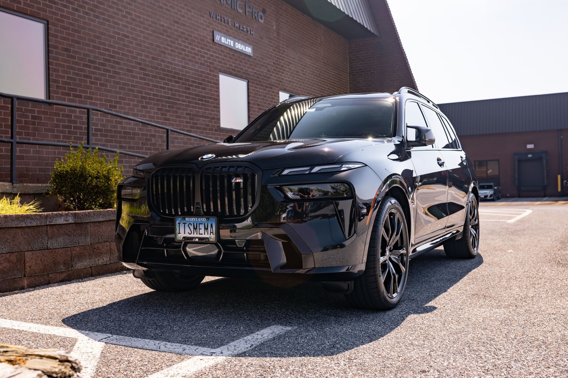 A shiny black BMW SUV parked in a brick building's parking lot on a sunny day.