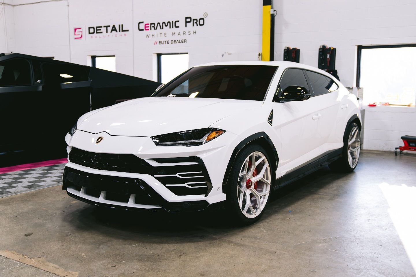 A white Lamborghini Urus SUV parked inside a workshop with Ceramic Pro branding on the wall.
