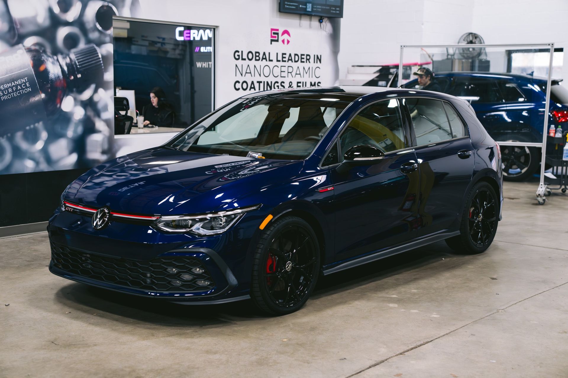 A dark blue Volkswagen Golf GTI parked inside a garage next to a sign for nanoceramic coatings.