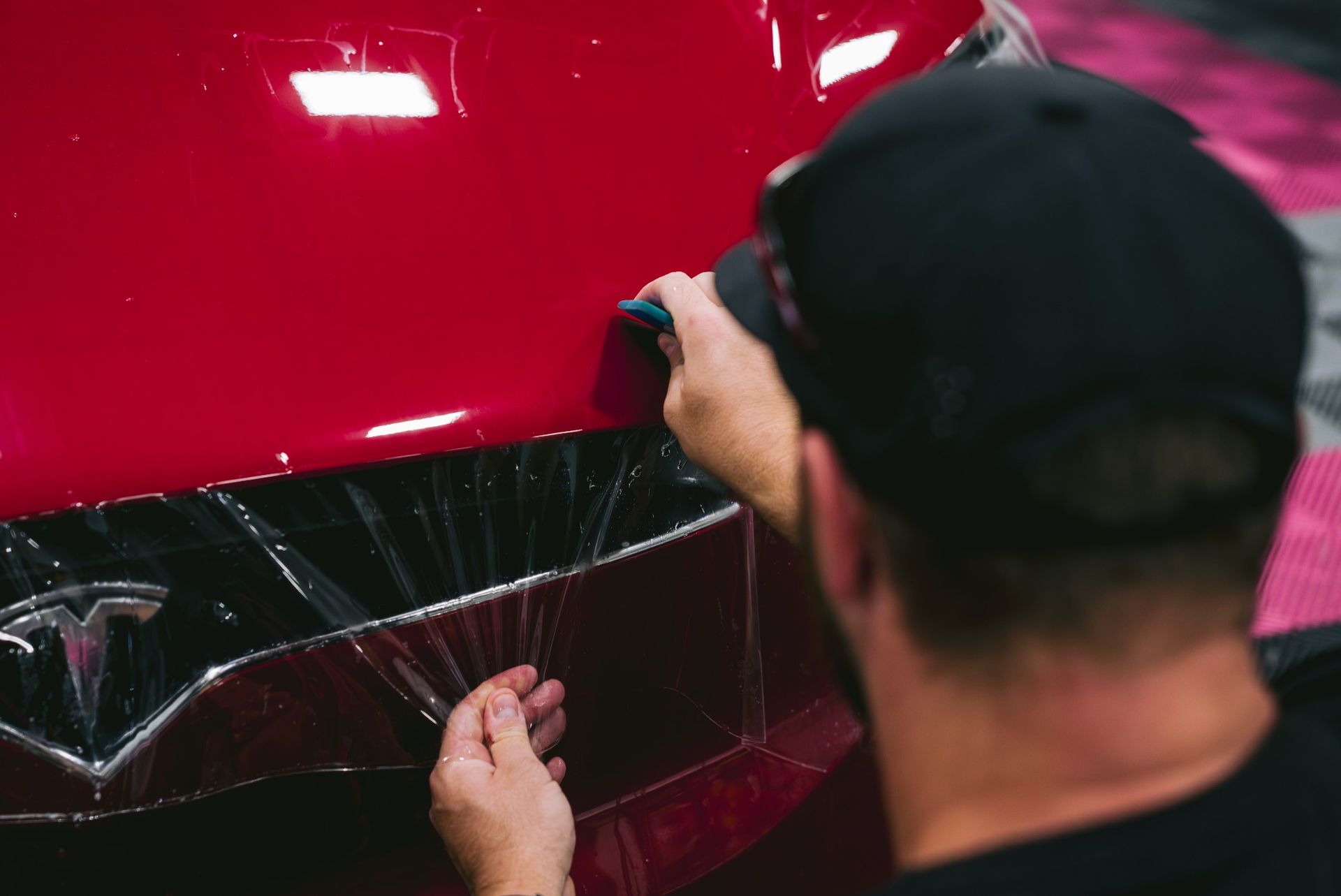 Technician installing paint protection film on red car to prevent scratches and damage