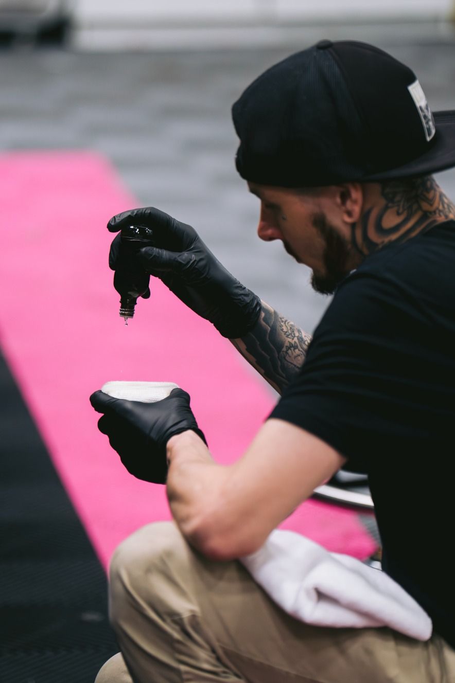Tattooed worker in black gloves holding a paint brush beside a bright pink surface