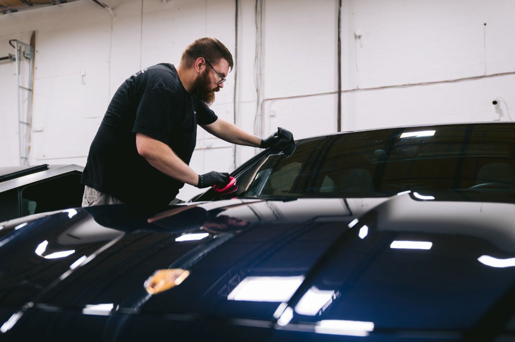 Person polishing a black car in a garage with a buffer tool