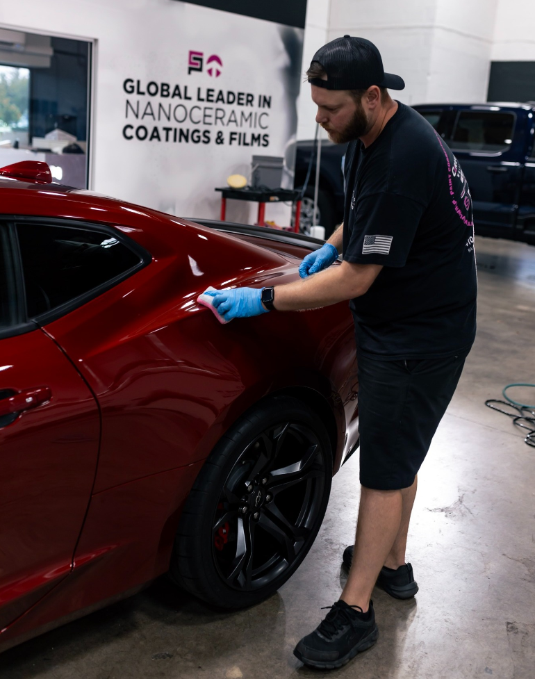 A man is polishing a red car in front of a sign that says global leader in nanoceramic coatings & films