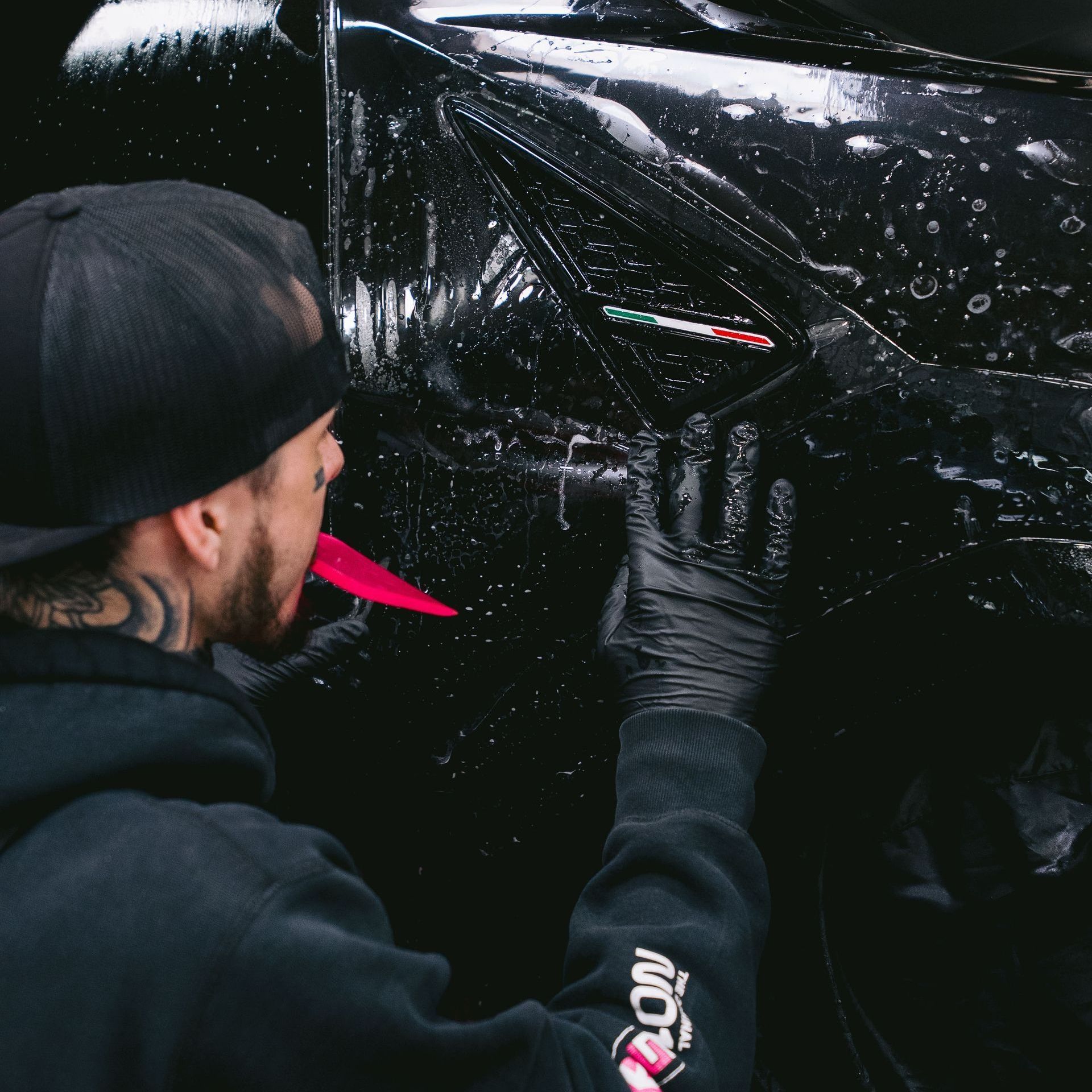 A person wearing black gloves is polishing the hood of a red car.
