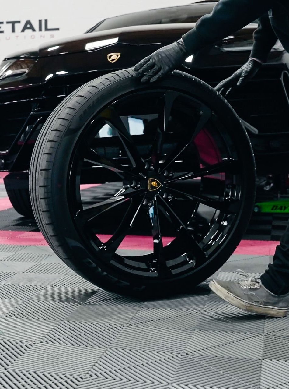 A person wearing black gloves is polishing a black car