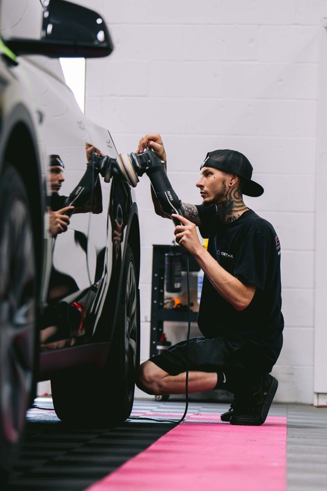 A man is cleaning the wheel of a black car with a sponge.