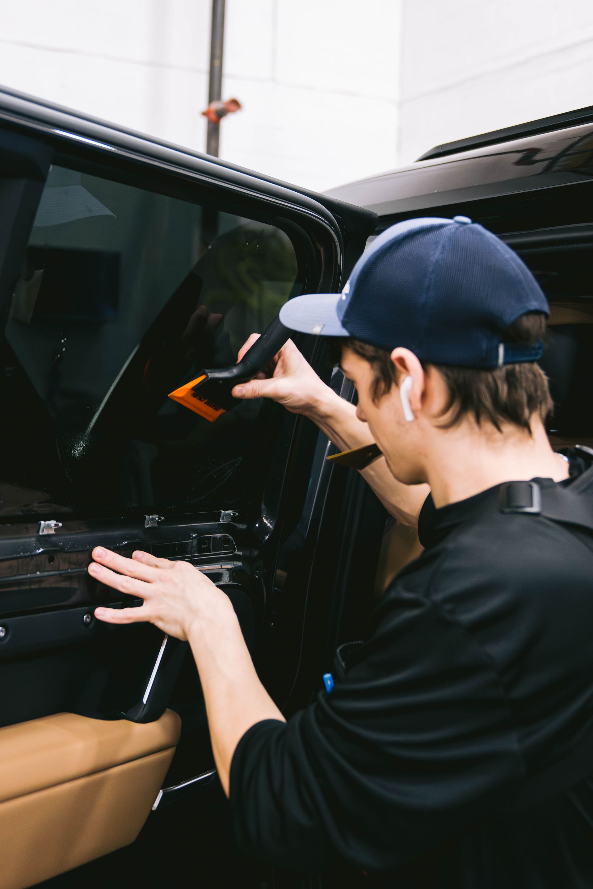 A man in a baseball cap is applying window tinting to a car window.