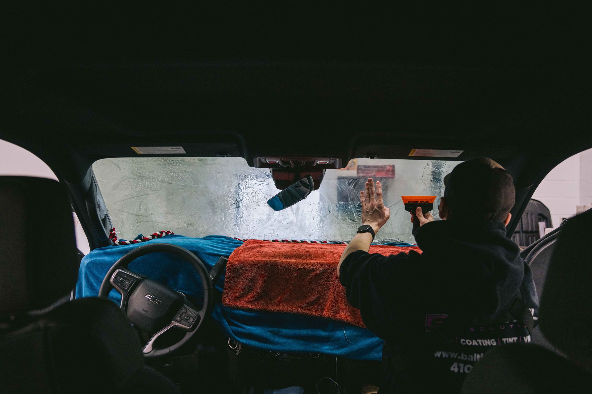 A man is applying window tinting to a car windshield.