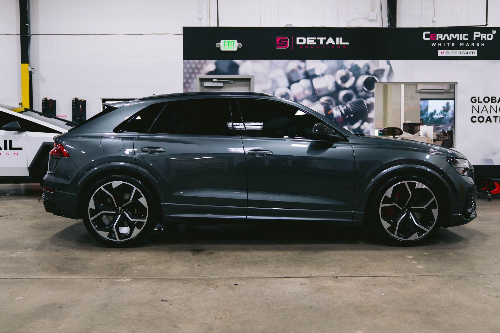 A gray car is parked in a garage next to a white car.