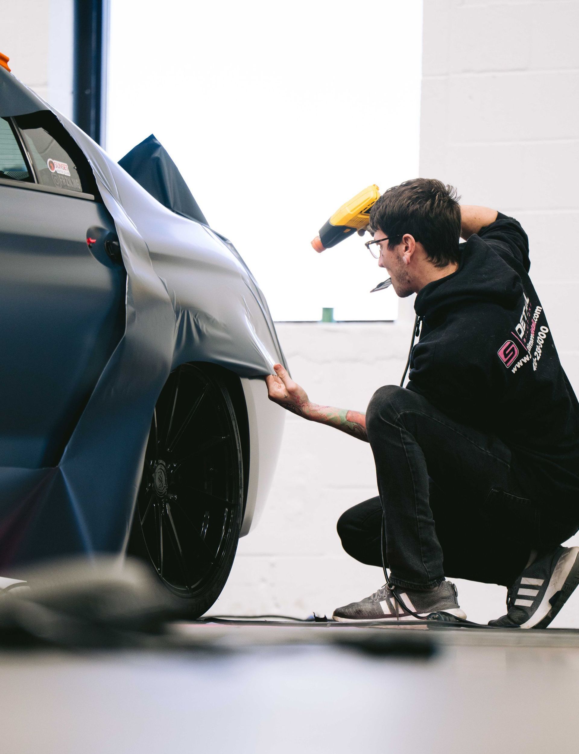 A person wearing black gloves is polishing a black car