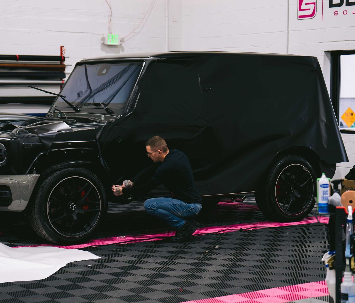 A man is working on a black jeep in a garage.