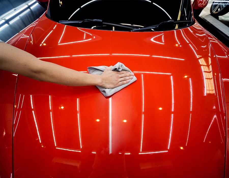 A person is cleaning the hood of a red car with a cloth.