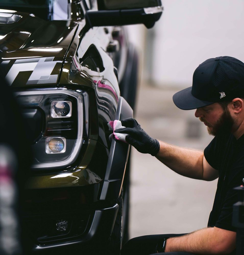 A man wearing a hat and gloves is polishing a car