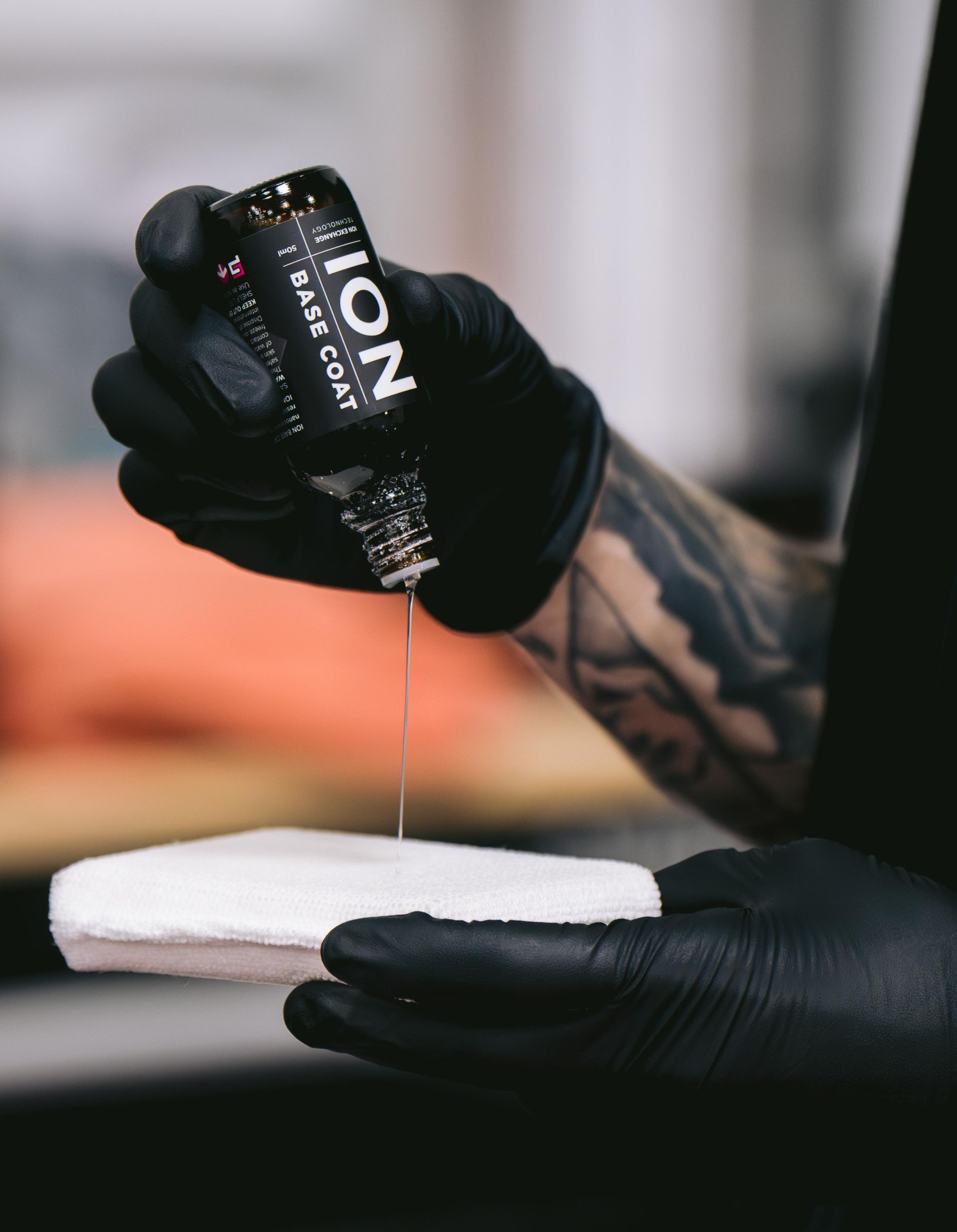 Person wearing black gloves, applying liquid from ION bottle onto a white pad.