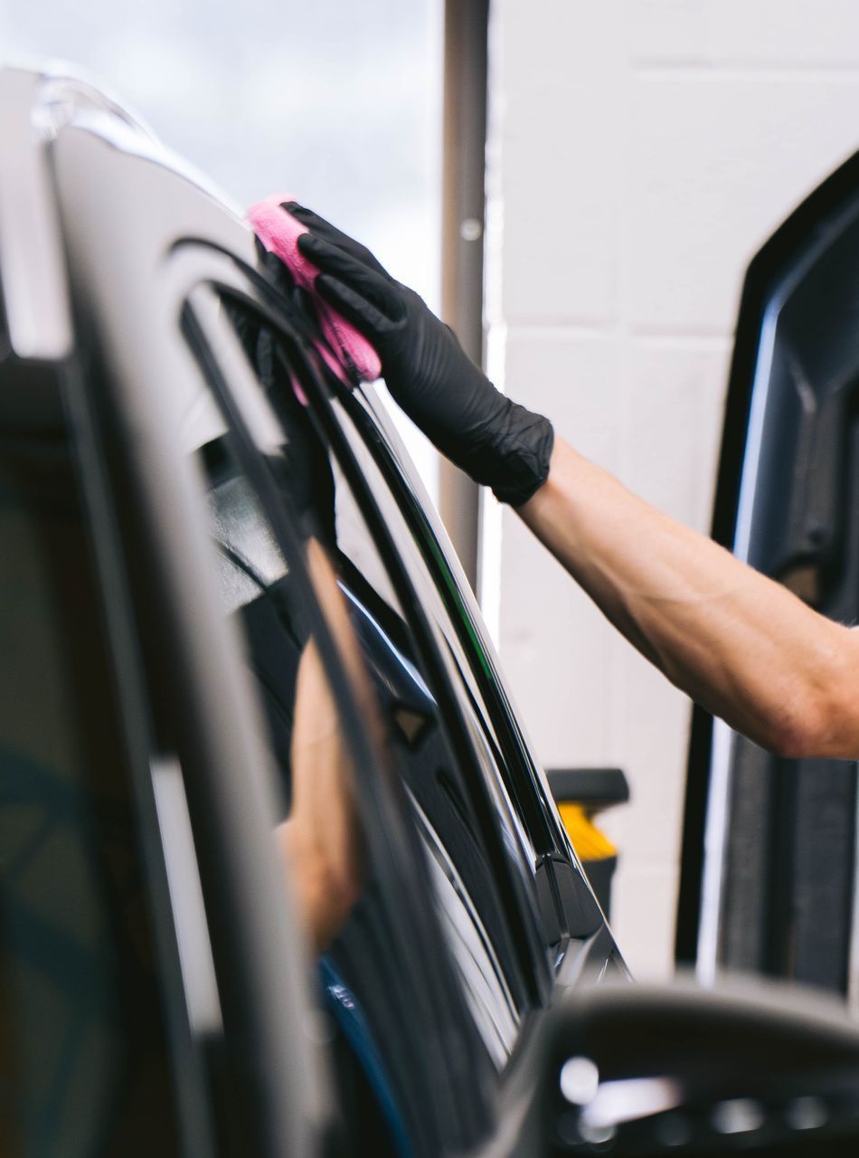 A person wearing black gloves is polishing a black car