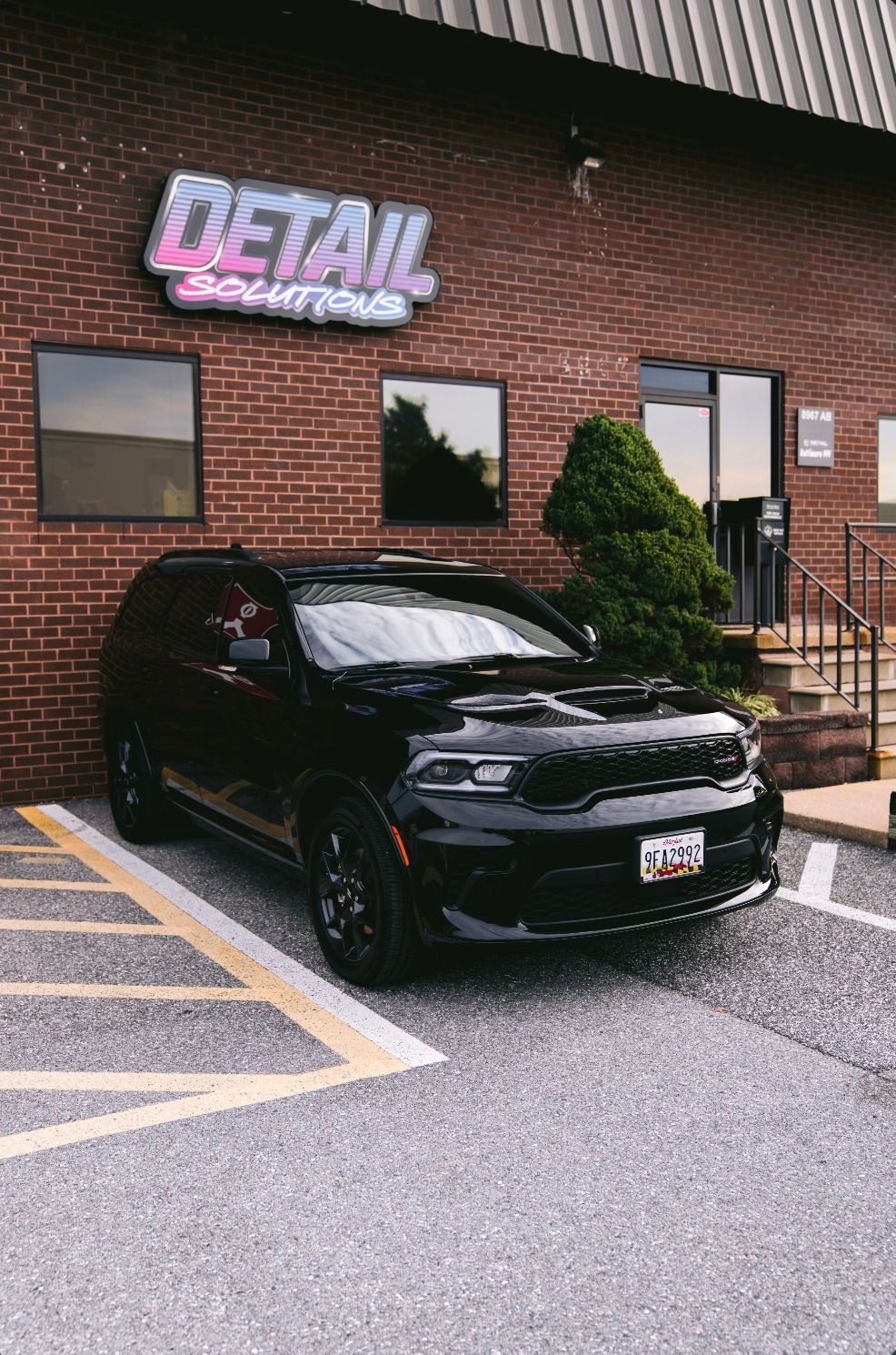 A dark grey Tesla Model Y parked on a checkered floor in a Ceramic Pro automotive detail shop.