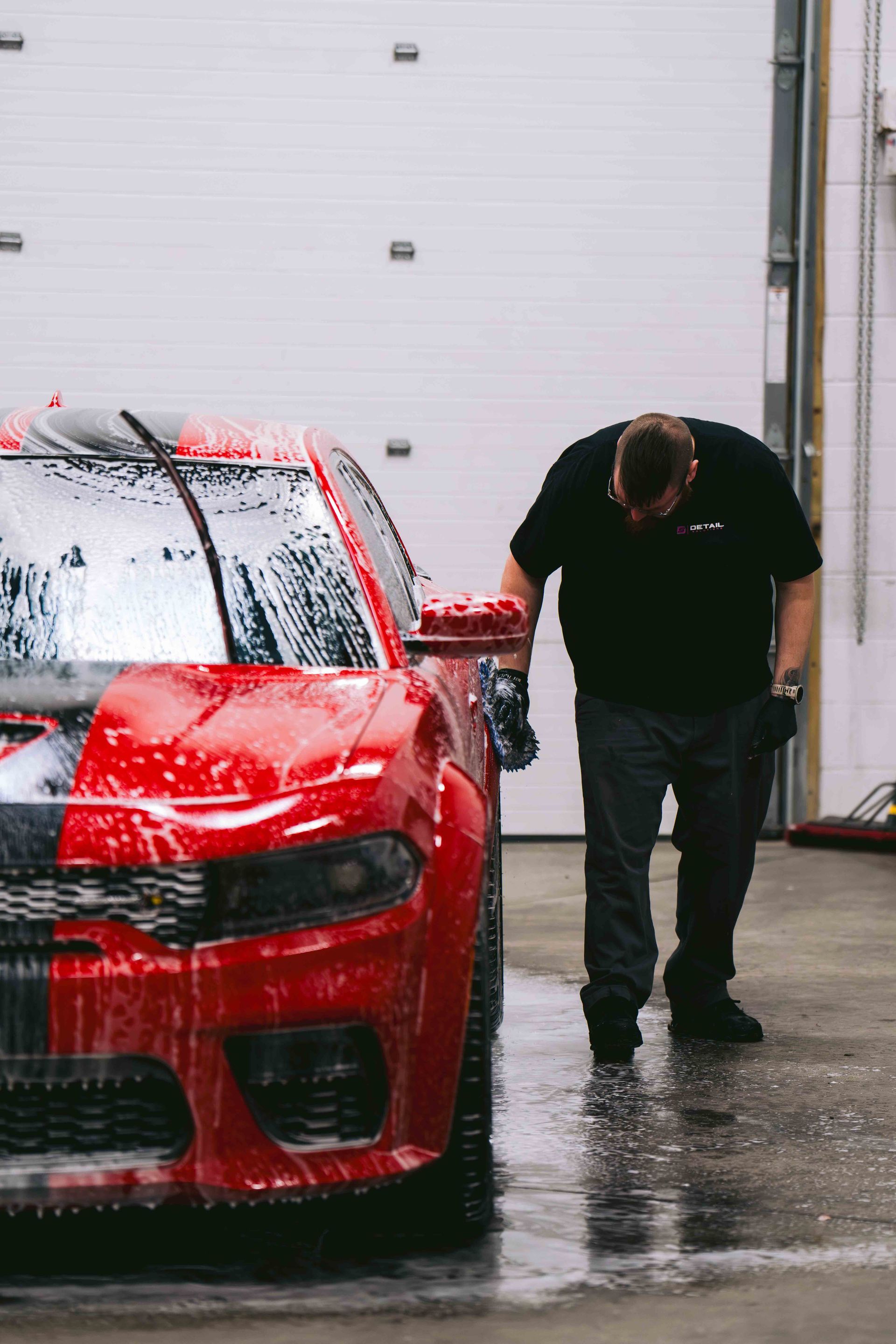 A man is washing a red car in a garage.