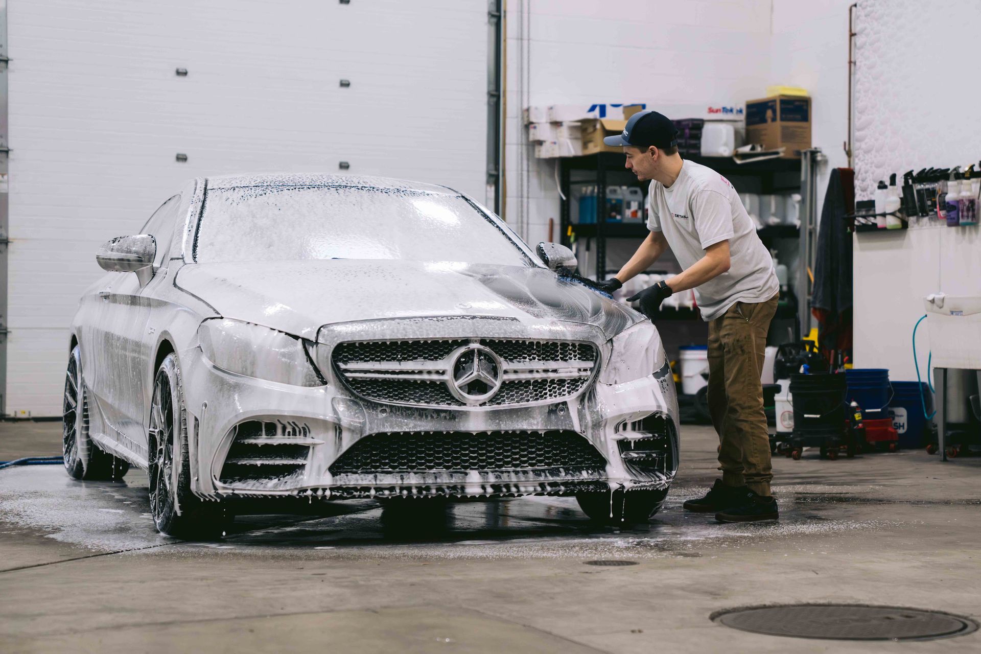 A man is washing a mercedes with foam in a garage.