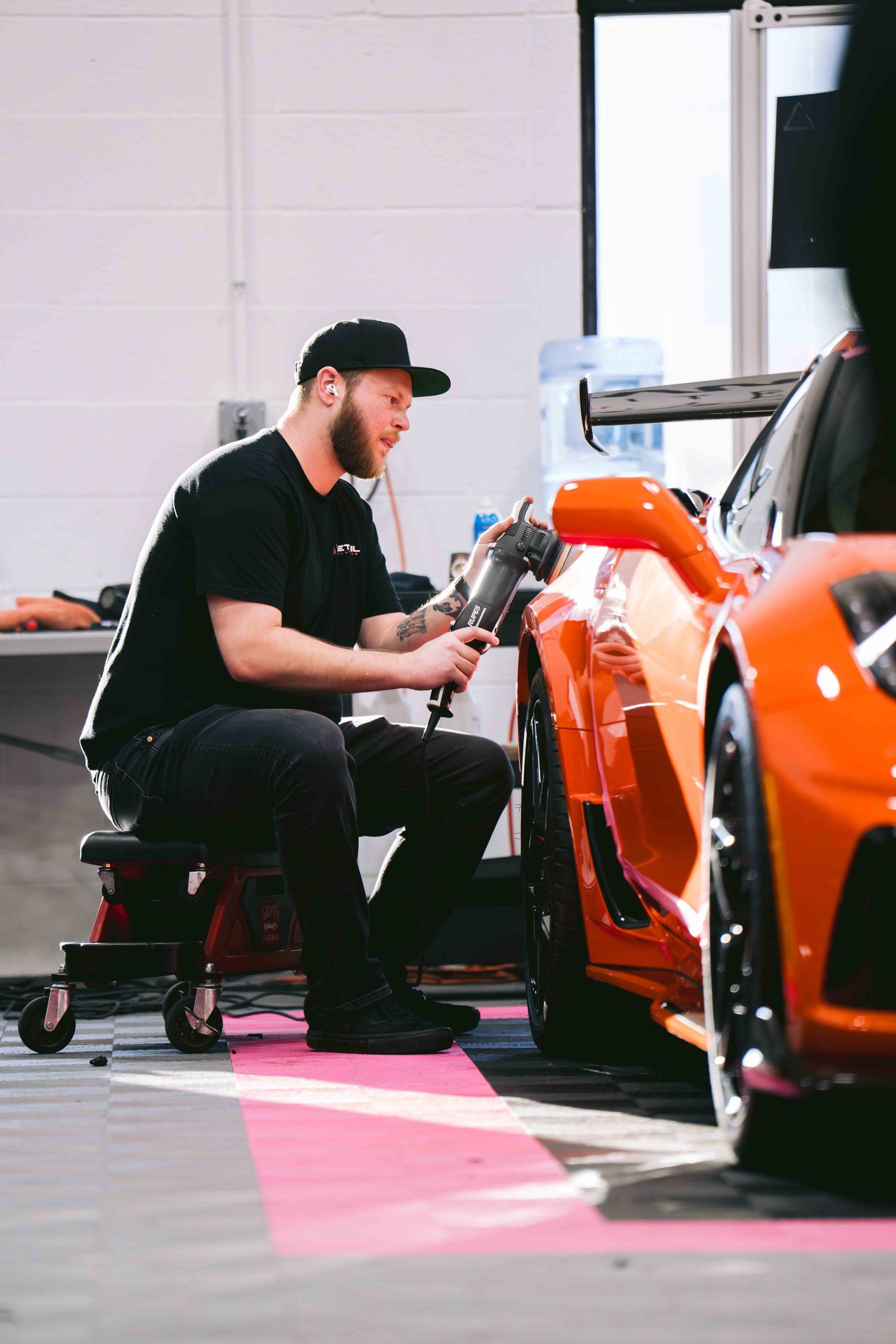 A person wearing black gloves is polishing a black car
