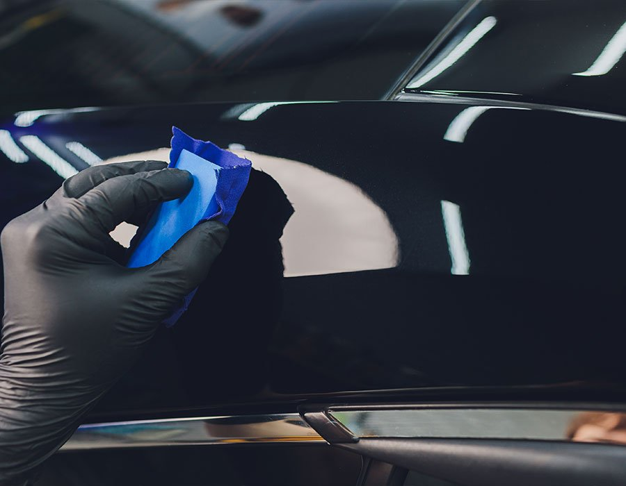 A person wearing black gloves is cleaning a car with a blue sponge.